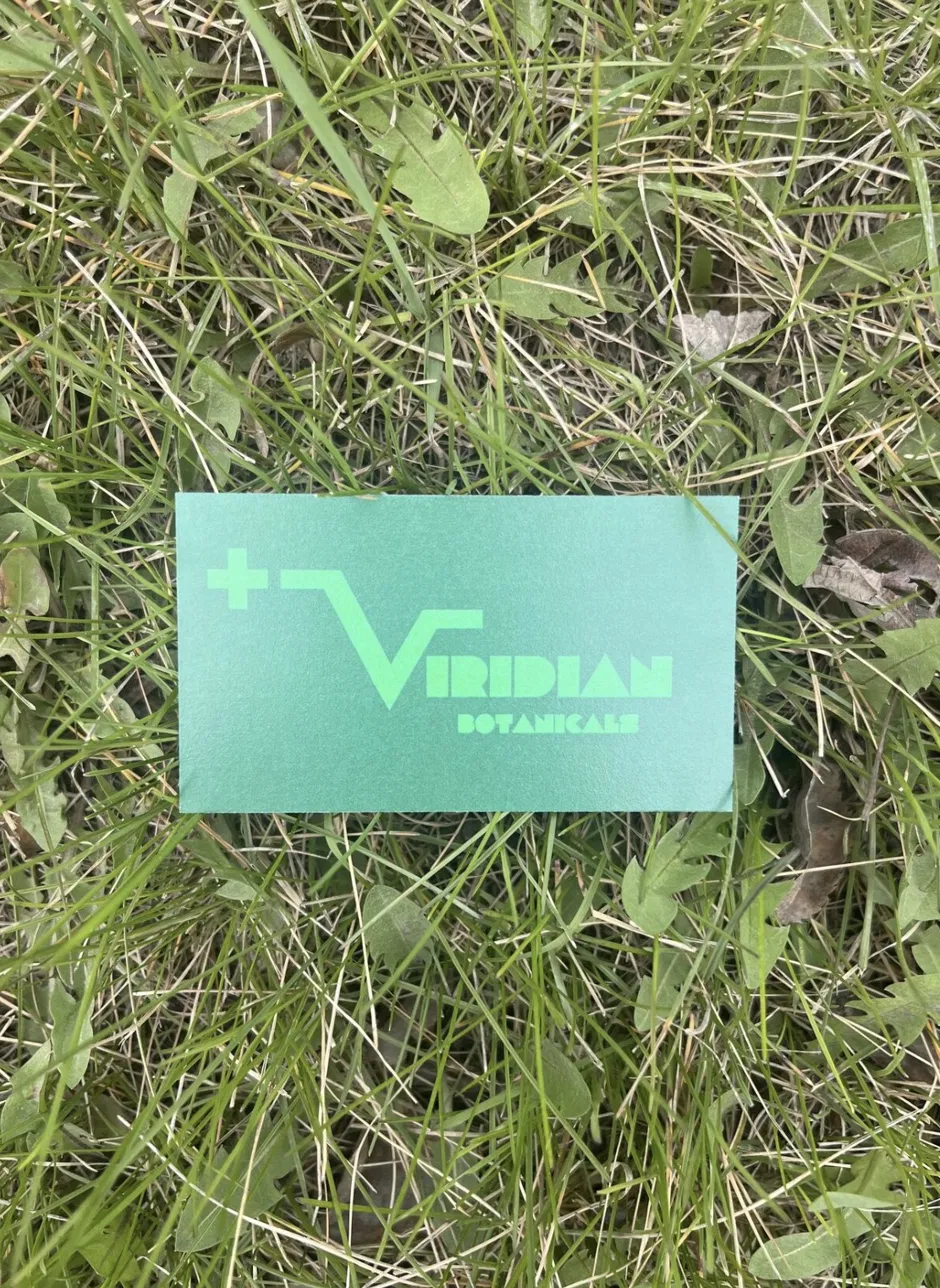 Viridian Botanicals business card laying on grass.