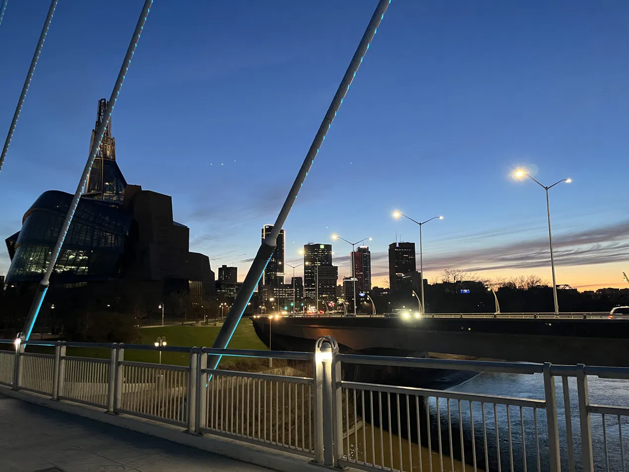 The Forks at dusk with the Canadian Museum for Human Rights, the river, and bridge cables in frame.