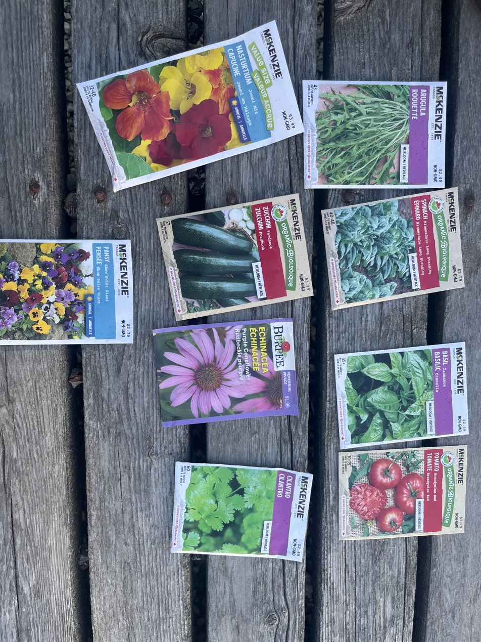 Heirloom seed packets laid out on weathered wood: Nasturtium, Pansy, Arugula, Spinach, Zucchini, Echinacea, Basil, Cilantro, Tomato.